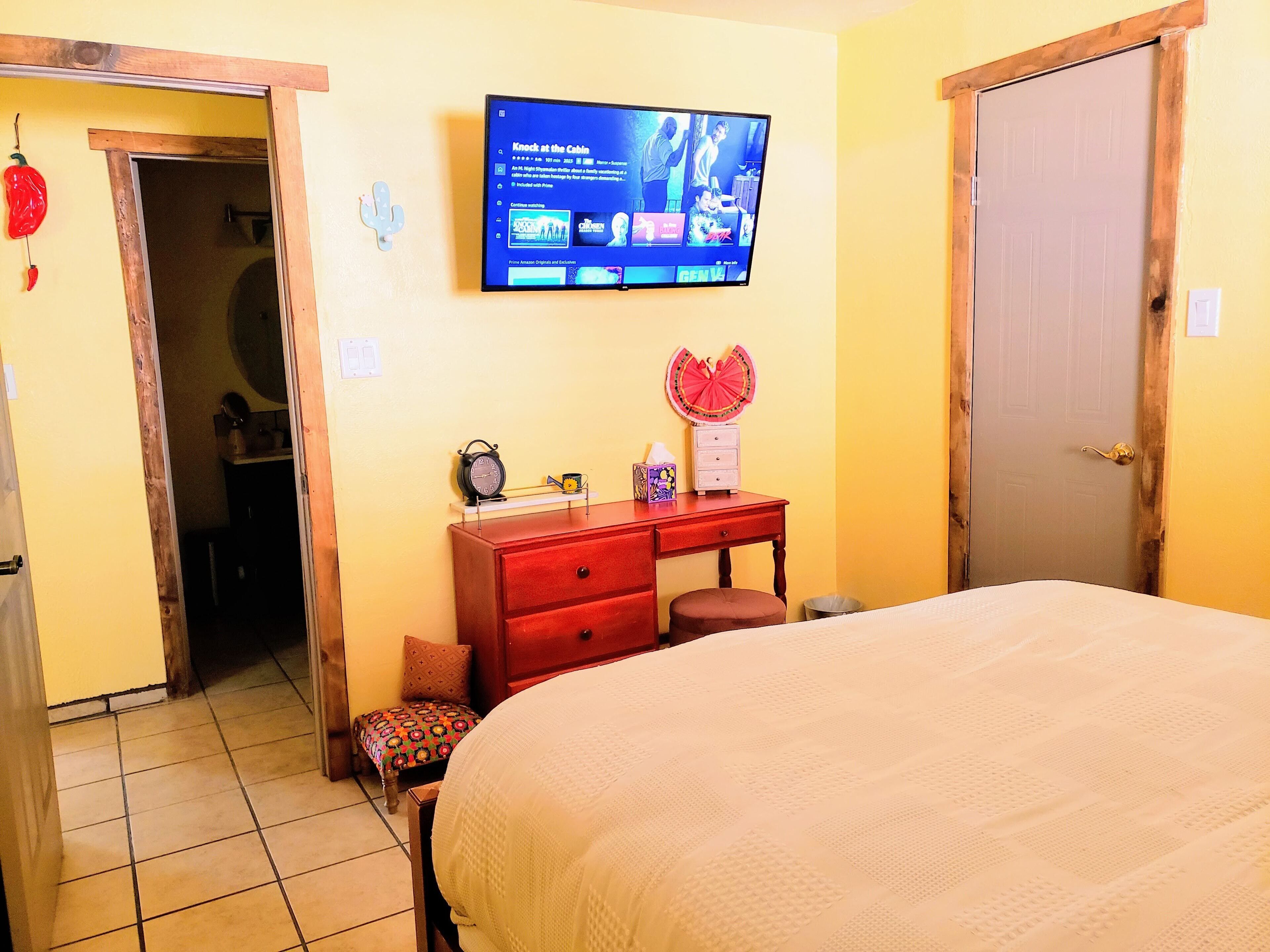 Una habitación de hotel con una cama, un televisor fijado a la pared, un escritorio de madera y una puerta.