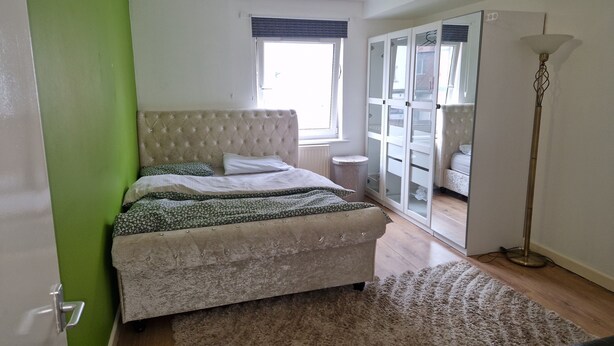 A bedroom with a bed, a green wall, a window, a wardrobe, and a floor lamp. - Remarkable 1-bed Apartment in Northampton Town cen (Northampton)