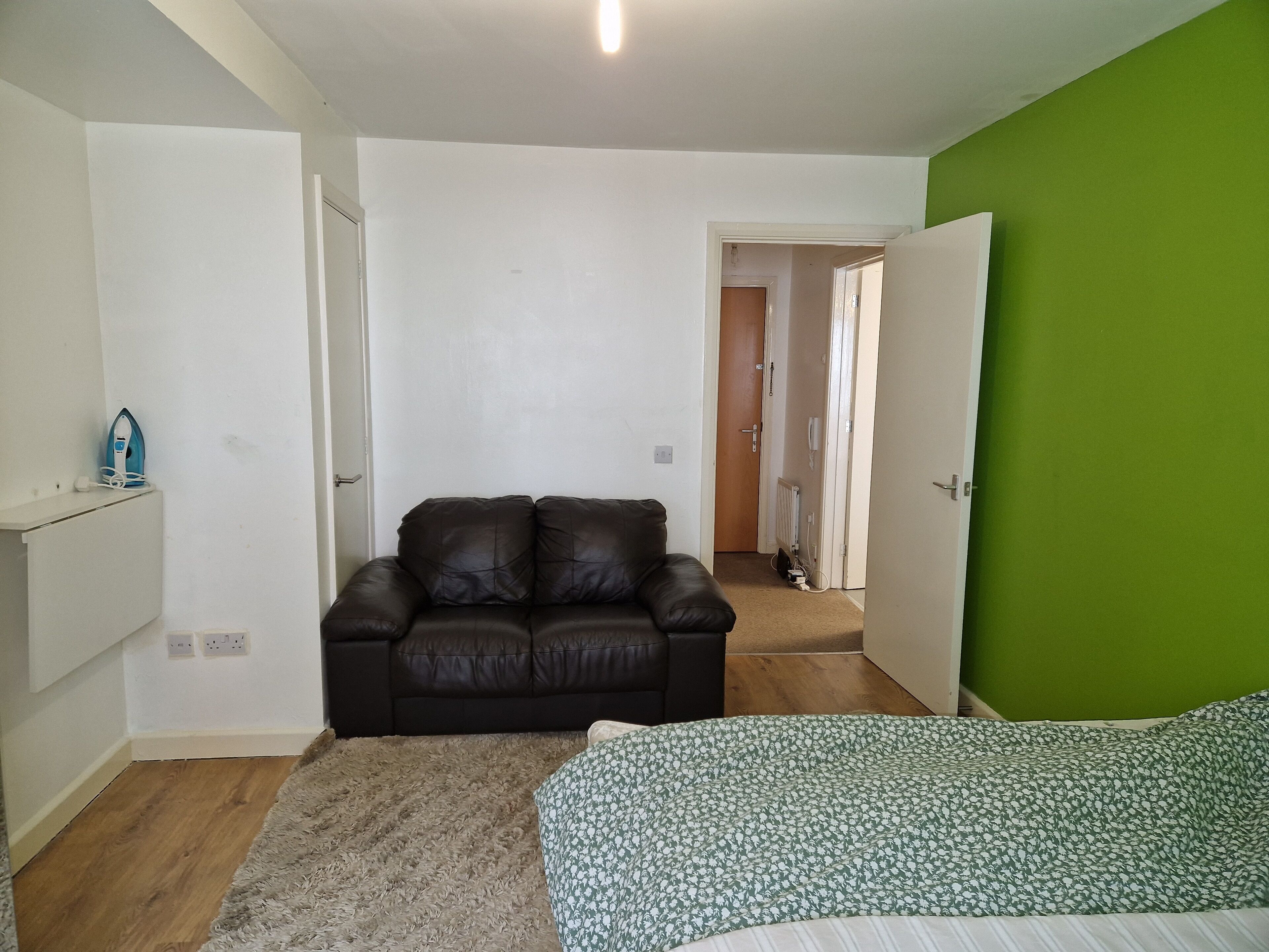 Quarto com sofá de couro marrom, cama estampada, parede verde e chão de madeira.