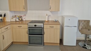 A compact kitchen with wooden cabinets, a built-in oven, a white refrigerator, and a bar stool. - Remarkable 1-bed Apartment in Northampton Town cen (Northampton)
