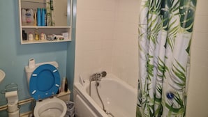 A bathroom with a toilet, sink, and bathtub. There is a shelf with toiletries and a mirror above the toilet. - Remarkable 1-bed Apartment in Northampton Town cen (Northampton)
