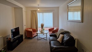 A living room with a black leather sofa, two red armchairs, a coffee table, and a TV on a black stand. - Remarkable 1-bed Apartment in Northampton Town cen (Northampton)