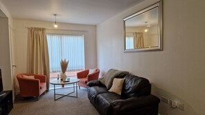A living room with a black leather sofa, a red armchair, a small round coffee table, and a large mirror on the wall. - Remarkable 1-bed Apartment in Northampton Town cen (Northampton)