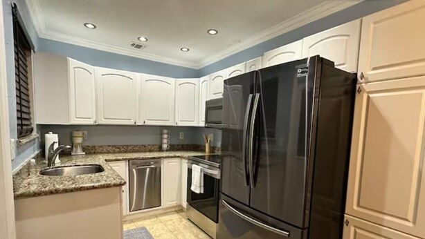 A kitchen with white cabinets, a black refrigerator, stainless steel appliances, and a granite countertop.