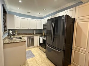 A kitchen with white cabinets, a black refrigerator, stainless steel appliances, and a granite countertop.