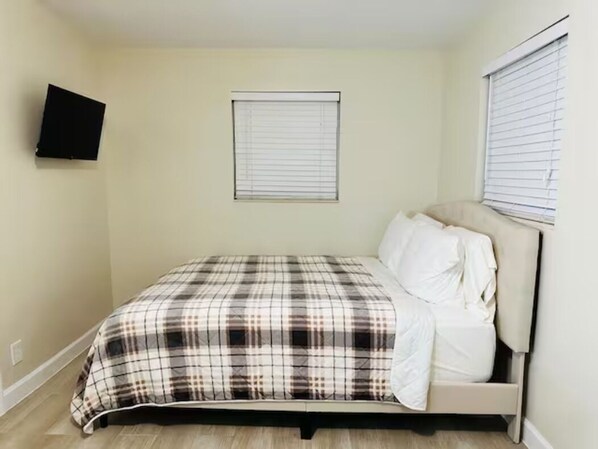 A bedroom with a bed, a television mounted on the wall, and a window with blinds.