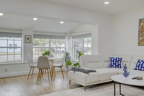 A modern living room with a white sofa, a coffee table, and a dining area with chairs and a table.
