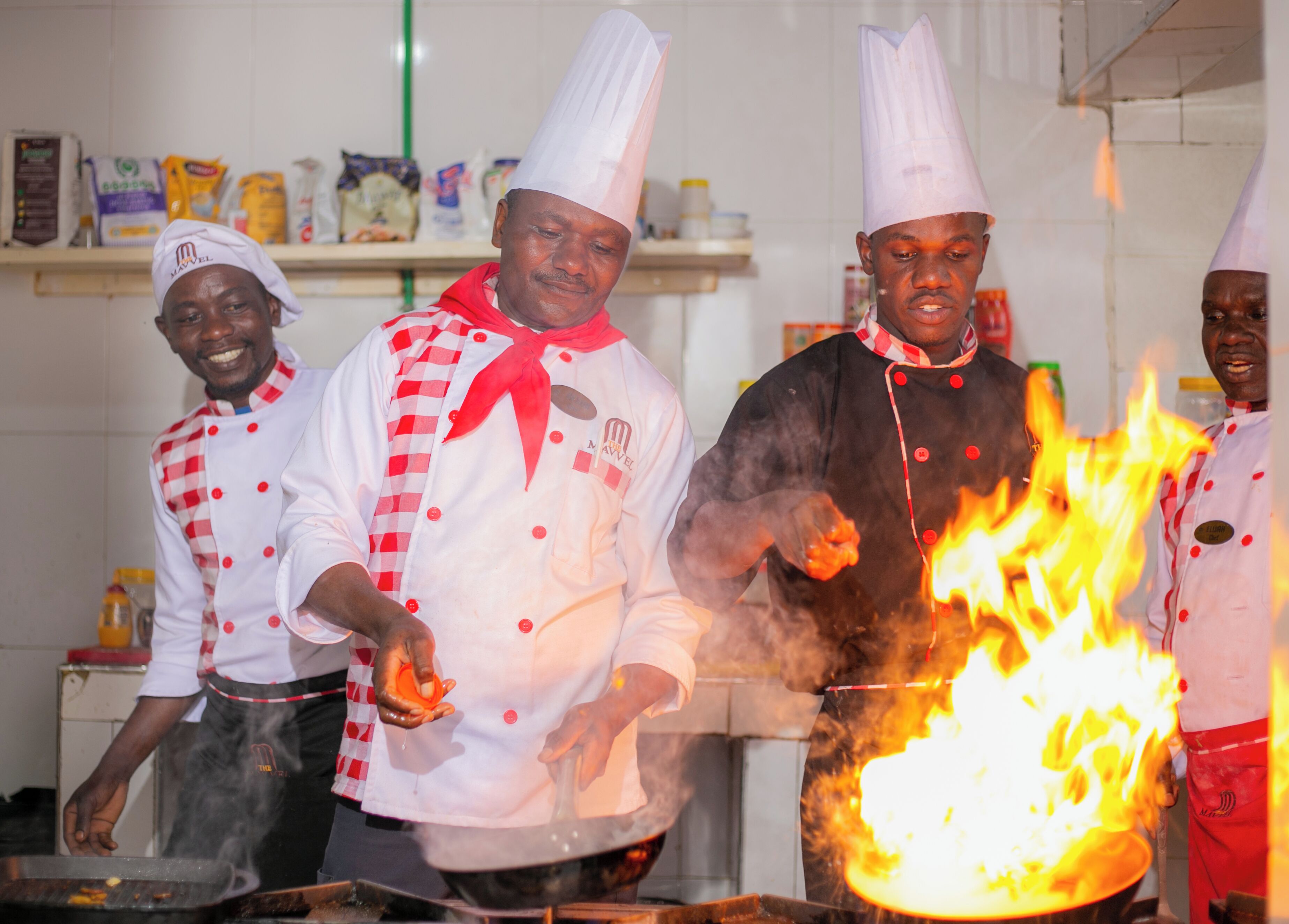 Chefs in a kitchen with a large fire.