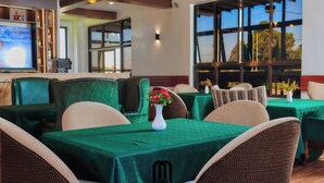 Un restaurante con manteles verdes, sillas de mimbre y un amplio ventanal con vistas.
