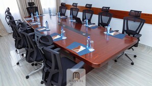 Un salón de conferencias con una larga mesa, sillas de malla negra, botellas de agua y un logotipo en la mesa.