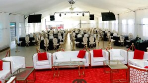Un amplio espacio interior con filas de sillas y mesas blancas, una alfombra roja y una araña de cristal.