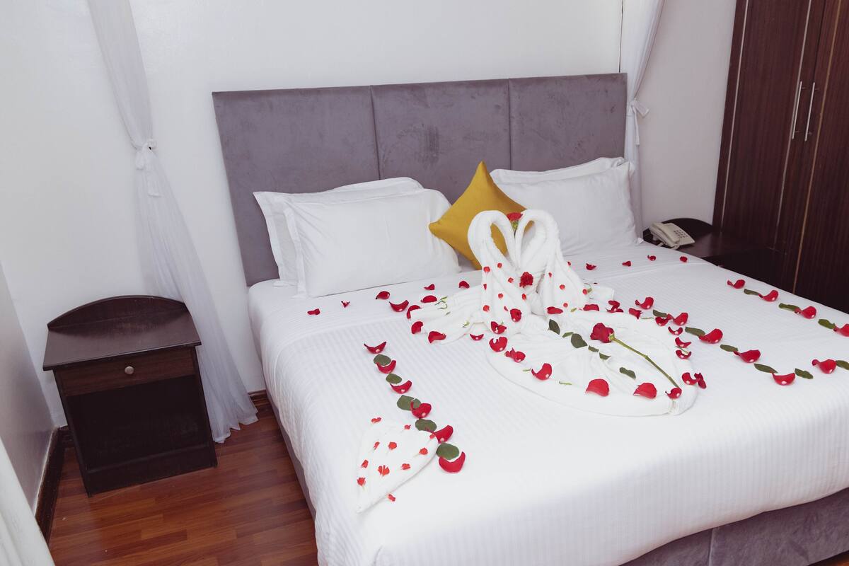 A neatly made bed with white linens, a single yellow pillow, and a white towel folded at the foot.