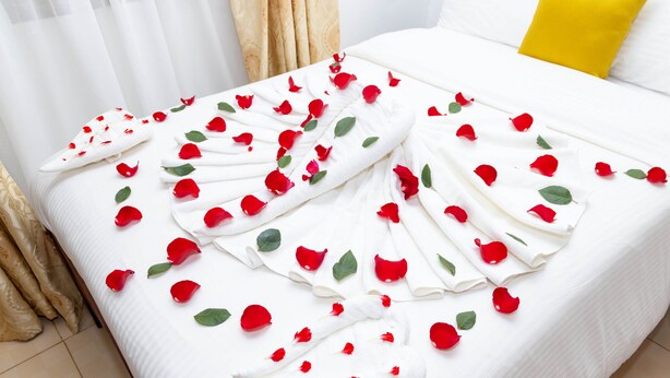 Una cama impecable con sábanas blancas y pétalos de rosa esparcidos.