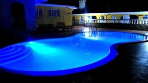 Una piscina con iluminación azul, rodeada por un edificio con una torre y un balcón.