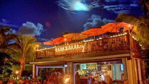An outdoor bar area with multiple tables and chairs, umbrellas, and a wooden deck overlooking a pool. - #4101 Fantastic 2-bed condo-Coral Gardens Resort (The Bight Settlement)