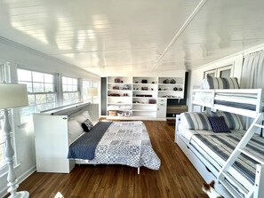 Una habitación amplia con una cama, un sofá, una estantería empotrada y un ventanal que deja entrar luz natural.