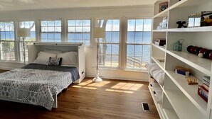 A bedroom with a bed, a nightstand, a lamp, a window with a view of the sea, and a bookshelf. - Life is better at the Lake 
Lakefront home that sleeps 13!  (Summerton)