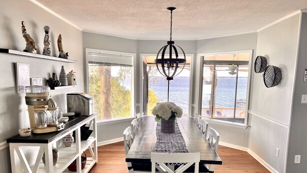 A dining room with a long table, white chairs, a chandelier, and a view of the water. - Life is better at the Lake 
Lakefront home that sleeps 13!  (Summerton)
