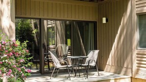 En udendørs terrasse med bord og stole, en skydedør i glas samt en træterrasse.