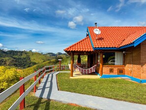 A house with a red-tiled roof, a wooden porch, and a view of green hills. - Pousada Dona Manoela (Gonçalves)