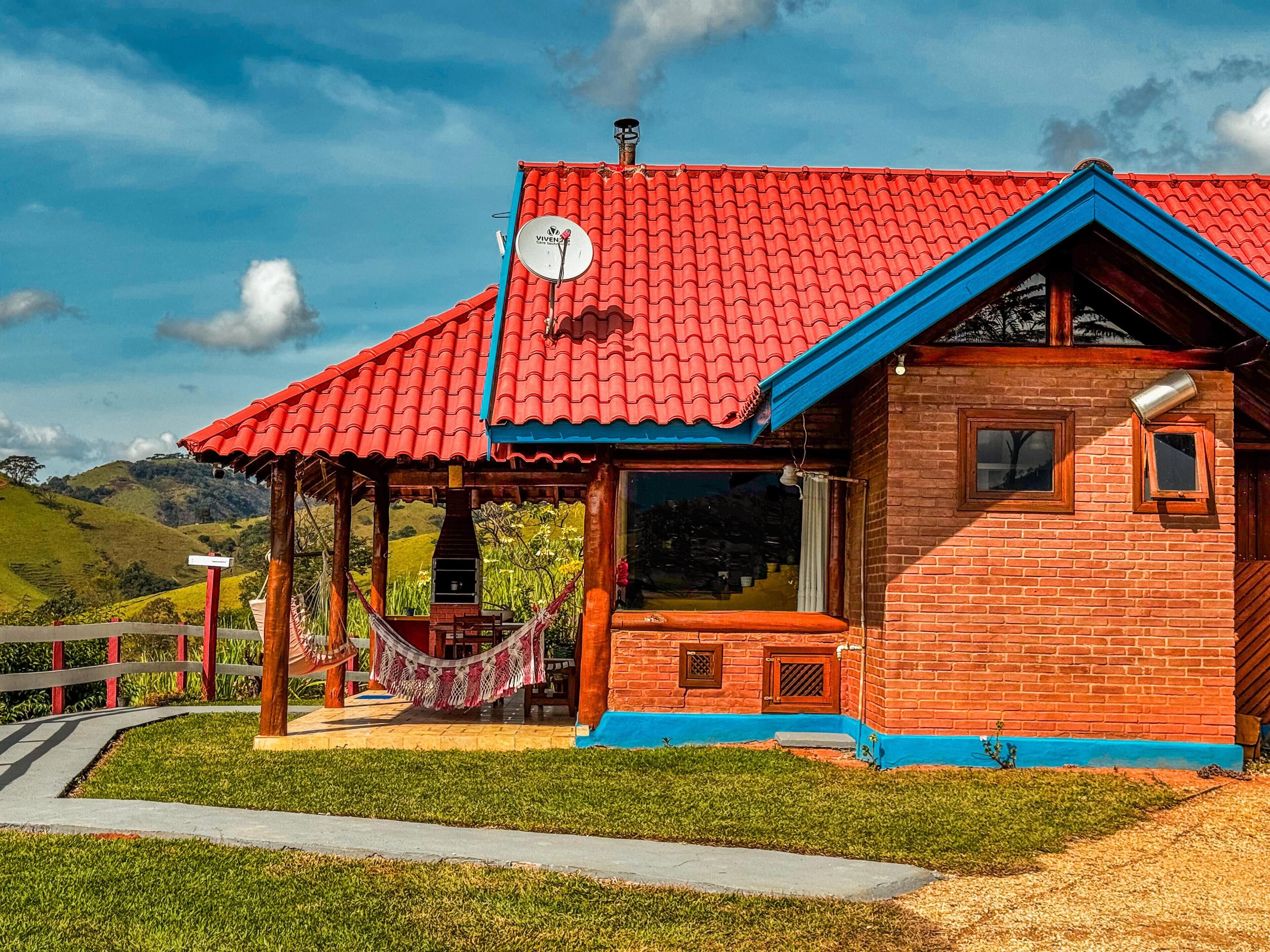 Una casa con techo rojo, detalles azules y fachada de ladrillo, además de una hamaca.
