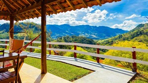 A wooden pergola with a hammock and a table, overlooking a mountainous landscape with a clear sky. - Pousada Dona Manoela (Gonçalves)