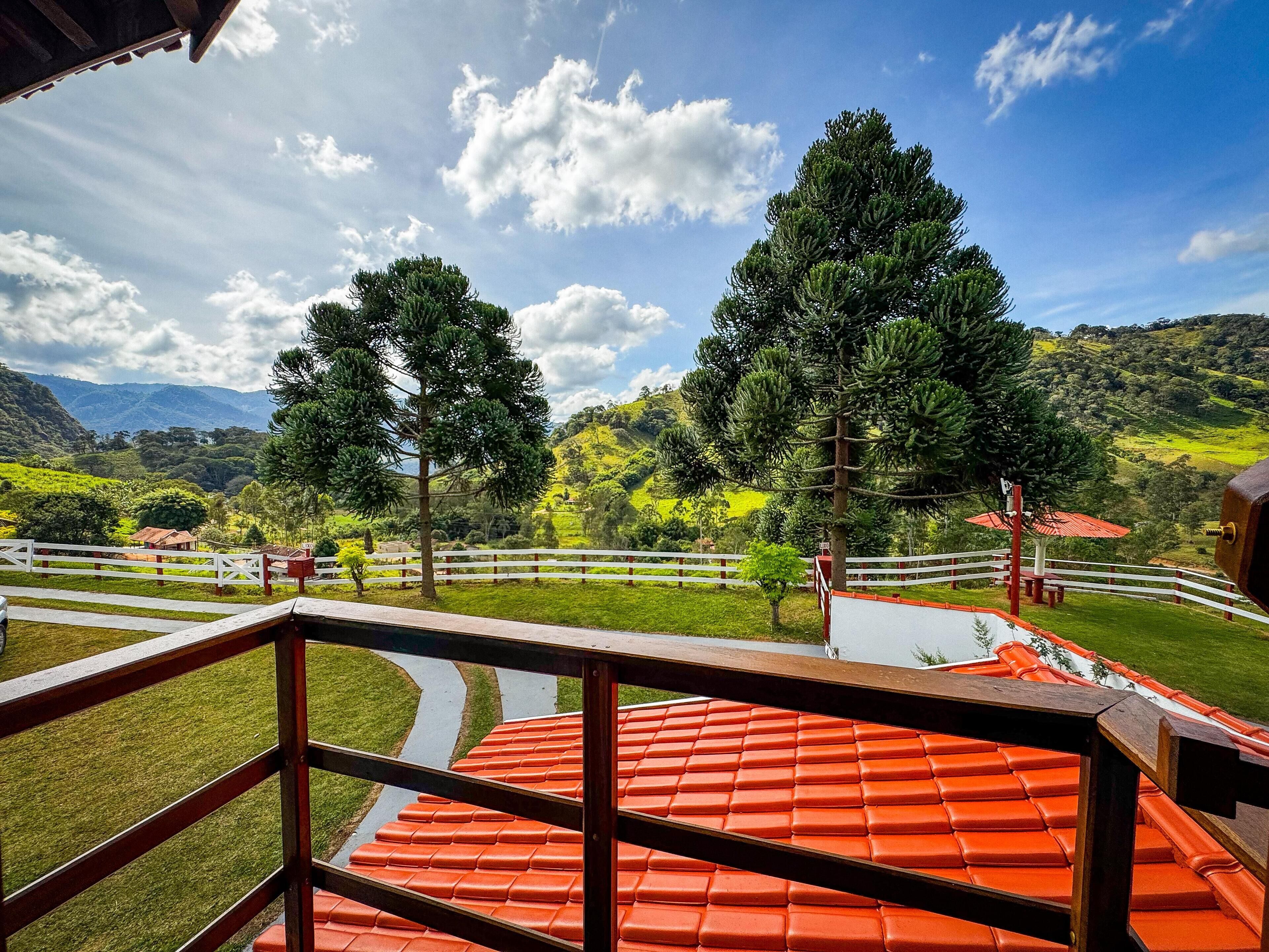 A terrace with a red-tiled roof, white railings, and a view of green hills and trees.