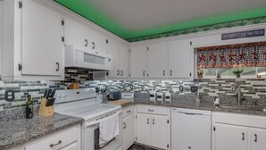 A kitchen with white cabinets, a microwave, a stove, and a sink. There is a green light on the ceiling, and a sign that says "Love, Laughter & Friends Always Welcome". - Green Acres House sleeps 6.  (Citra)