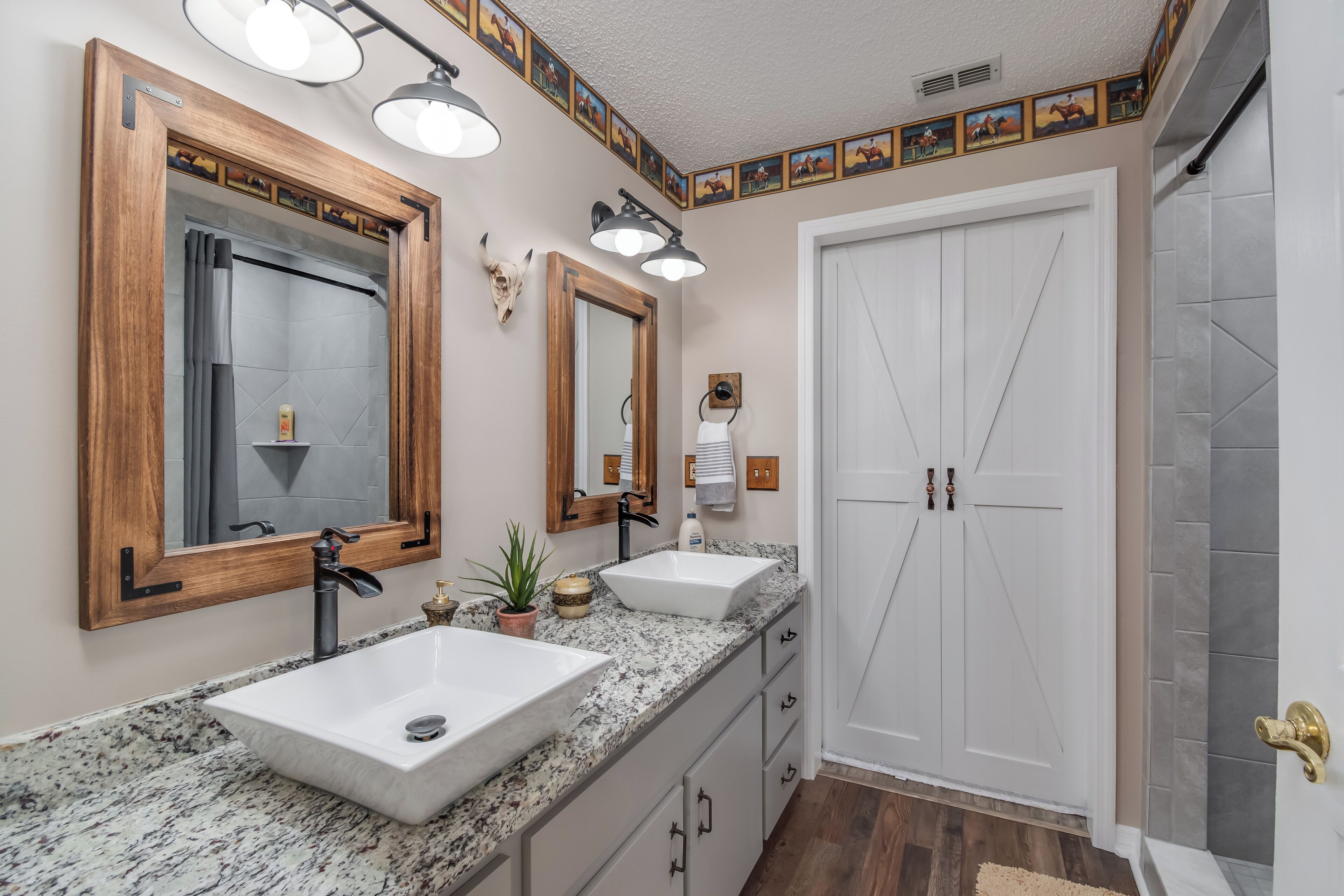 Une salle de bain avec deux lavabos, un grand miroir et une porte donnant sur l’espace douche.