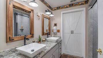Une salle de bain avec deux lavabos, un grand miroir et une porte donnant sur l’espace douche.