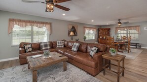 A spacious living room with a large sectional sofa, a wooden coffee table, and a dining area with a wooden table and chairs. - Green Acres House sleeps 6.  (Citra)