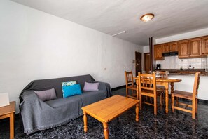 A compact living space with a sofa, a wooden table, and a kitchen area with wooden cabinets and a countertop. - Las Blanquitas 2 (Playa de Las Americas)