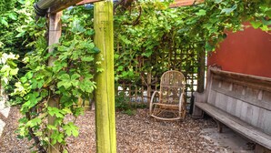 Una pérgola de madera con una silla de mimbre debajo, rodeada de follaje y grava.