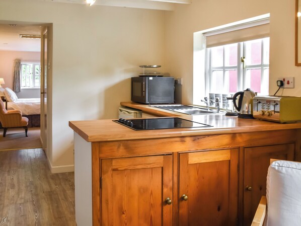 A compact kitchen with wooden cabinets, a microwave, a toaster, and a kettle. - Little House on the Common (Diss)