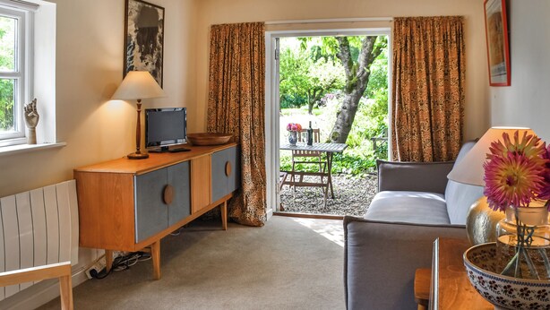 Una habitación acogedora con un sofá, un mueble de madera con televisor y una zona de comedor con mesa y sillas.