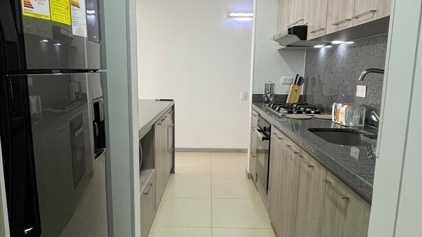 A modern kitchen with stainless steel appliances, light wood cabinets, and a tiled floor. - Apartamento de 2 Habitaciones en Cali (Cali)