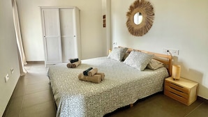 A spacious bedroom with a large bed, a bedside table, a mirror, and a wardrobe.