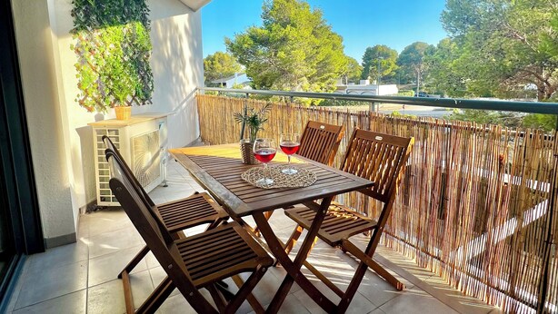 A wooden table with two chairs on a balcony, a wicker basket, and a glass of red wine.
