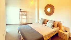 A bedroom with a bed, bedside tables, a hanging light fixture, and a wall-mounted mirror.