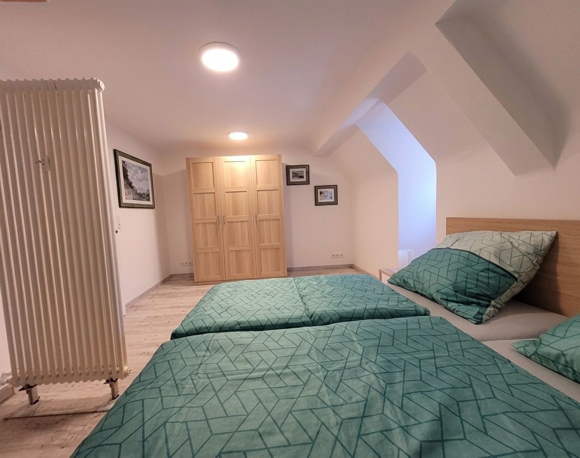 Ein Schlafzimmer mit zwei Betten, einem Holzschrank und einer schrägen Decke.