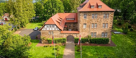 Ein großes Steinhaus mit rotem Dach, umgeben von üppiger Vegetation und einem gepflegten Rasen.