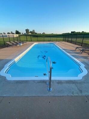 A rectangular swimming pool with a clear blue water surface, surrounded by a wooden deck and a metal railing.