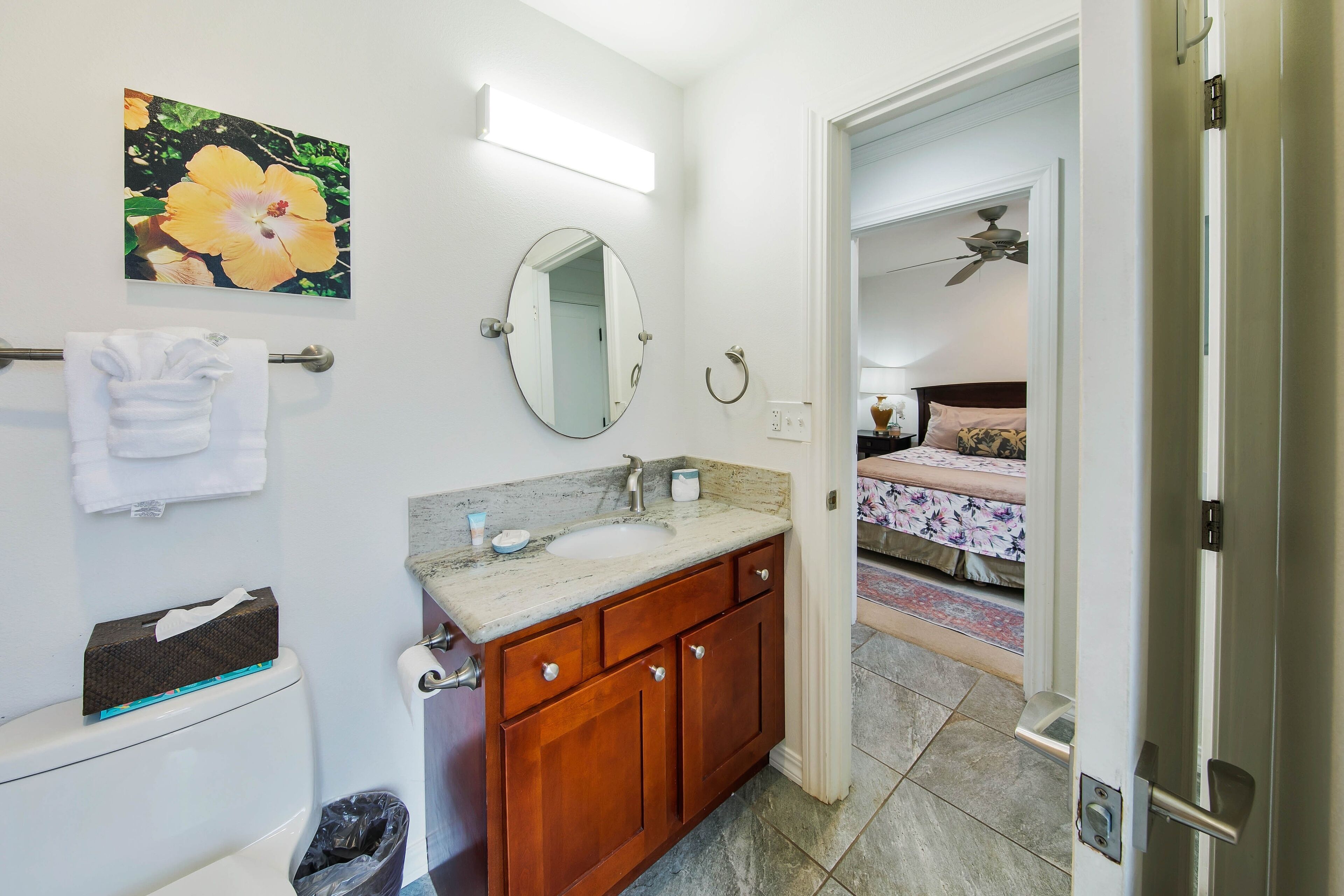 A bathroom with a sink, mirror, and toilet. There is a towel rack with towels and a trash can.