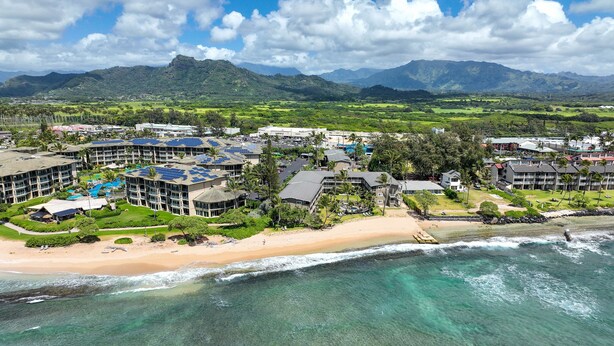 Un resort con varias construcciones, una playa y una cadena montañosa al fondo.