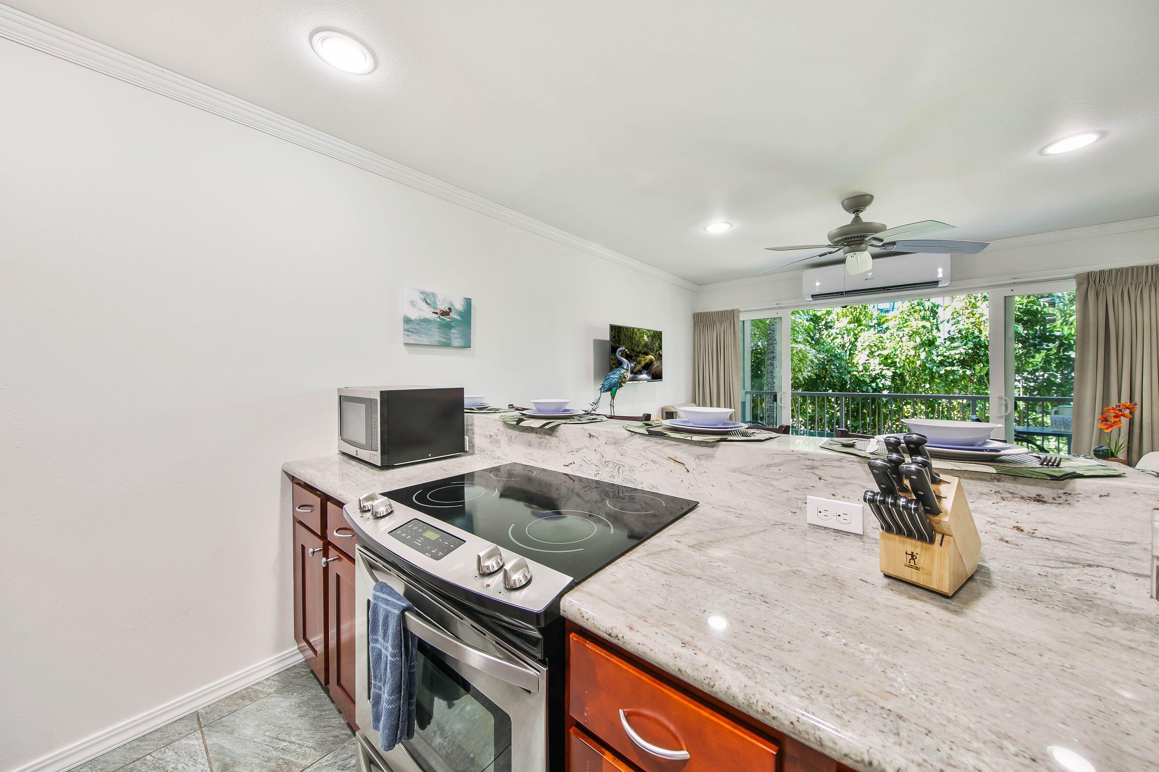 A modern kitchen with a built-in stove, oven, and microwave, a large island with a knife block, and a view of the outdoors through large windows.