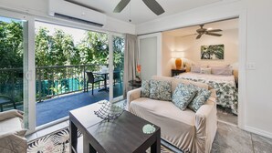 Una habitación con balcón, sofá, mesa y cama con ropa de cama floral.