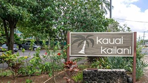 Letrero de 'kauai kailani' con un gráfico de palmera, rodeado de jardines ajardinados y un muro de piedra.