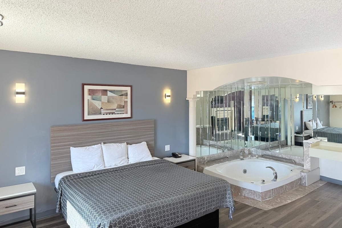 A modern bedroom with a large bed, a glass-enclosed shower, and a bathroom with a bathtub.
