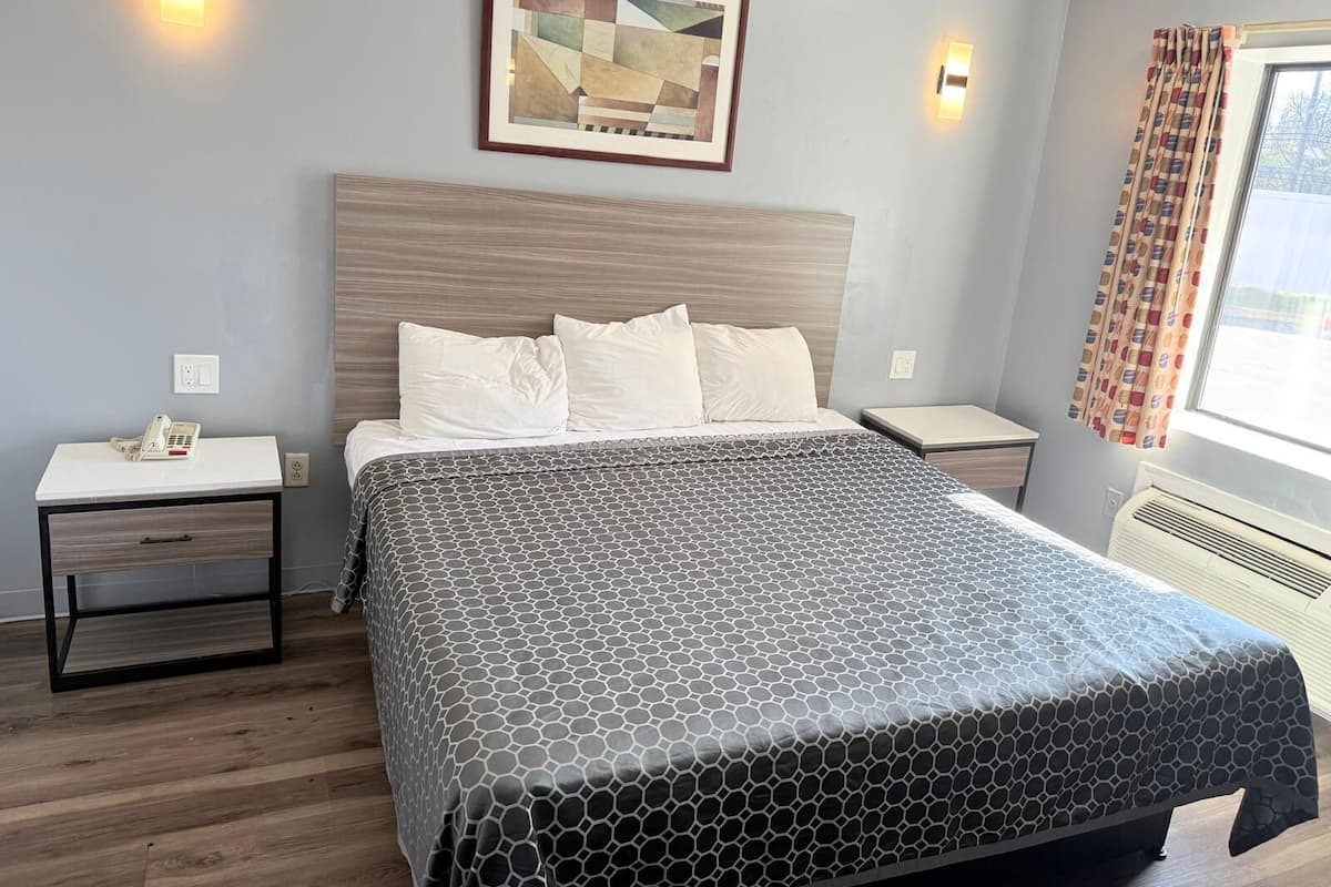 A hotel room with a large bed, a bedside table with a phone, a wall-mounted artwork, and a window with curtains.