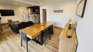 Una sala de estar moderna con una mesa de comedor de madera, un sofá tapizado en negro y un televisor de pantalla plana montado en la pared.